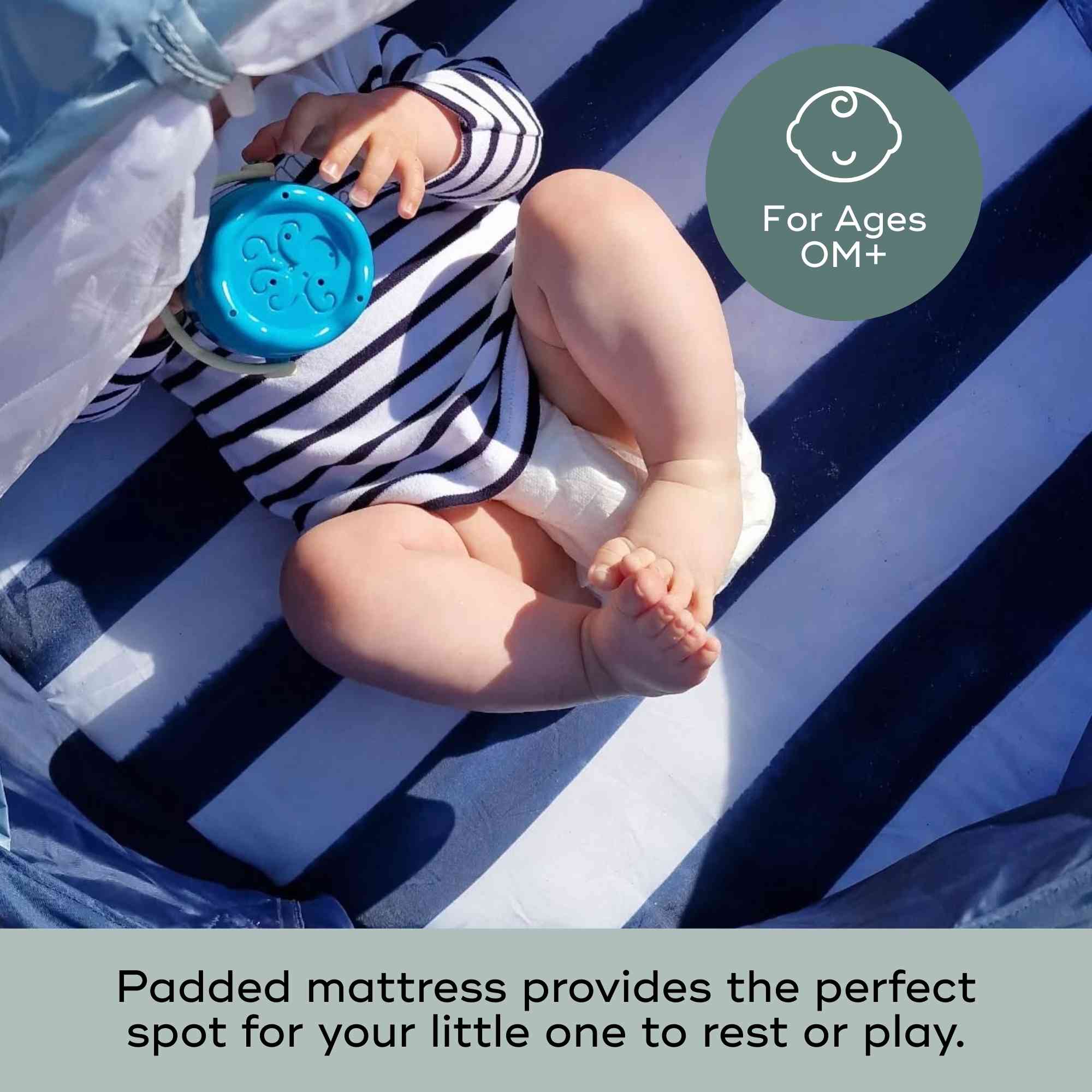 Baby sitting on a striped blue and white mat in pop up tent with a blue cup, wearing a striped outfit.